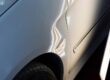 Paintless dent repair concept. Close up on dent behind the back passenger side door of a white sedan.